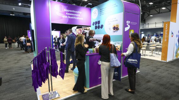 Gateway Qualifications stand at ATC. The stand has three walls and is open at the front with a counter. The stand is busy with people and a purple delegate bags are hung on a rack at the front.