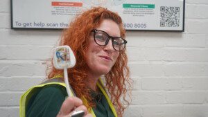 A student in high vis with red hair is smiling holding up a plug.